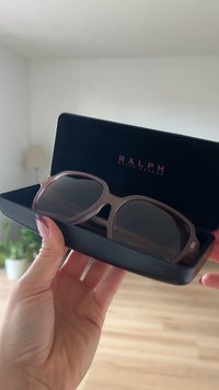 Ruske aurinkolasit, joissa on suuri, neliömäinen kehys mustassa kotelossa, jossa on kultainen logo ja tummat linssit; sileä pinta, jossa on kiiltävä viimeistely.