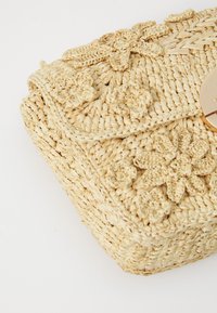 Geantă din paie țesută cu detalii florale, culoare bej natural, formă rectangulară, închidere plată și suprafață texturată. Dispune de un închizător rotund.