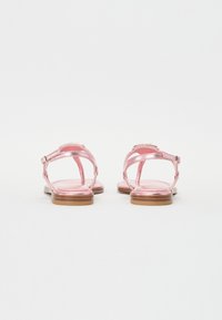 Rosa metalliska sandaler med platt sula, som har justerbara ankelremmar och en minimalistisk design. Slät yta, inga mönster eller metalliknande detaljer.