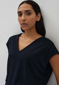 Marineblauwe, korte mouwen top met een V-hals ontwerp. Glad, lichtgewicht materiaal met een losse pasvorm en geen zichtbare patronen of accenten.