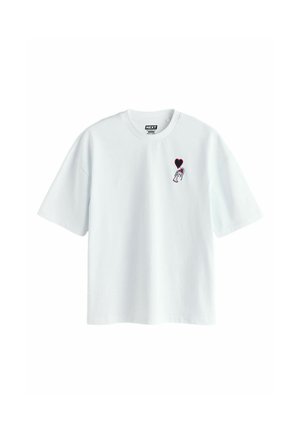 Bílé tričko s krátkým rukávem a malou grafikou ruky držící balón ve tvaru srdce na levé straně hrudi.