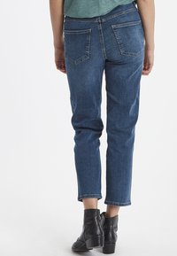 Vaqueros de mezclilla azul oscuro con un corte recto, que presentan bolsillos traseros y una longitud ligeramente recortada, combinados con botines negros.