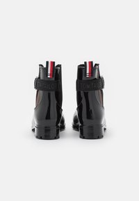 Bottines en cuir verni noir avec une languette, dotées d'une bande accenturée rouge et blanche et d'une bande texturée étiquetée "TOM TAILOR".