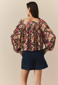 Bluză florală cu mâneci puff, având un fundal închis și flori de culoare roz aprinsă, galbenă și albă, asortată cu șorturi din denim închise.
