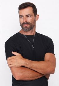 Sort kortærmet skjorte båret af en mand med en sølvvedhæng. Vedhænget er cylindrisk med et let vertikalt design.