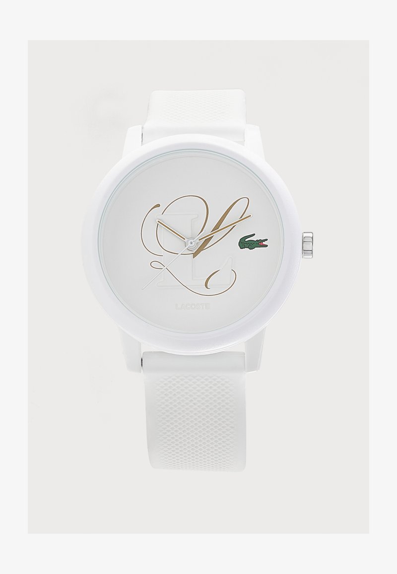 Montre-bracelet blanche avec bracelet en silicone texturé, initiales dorées en écriture cursive sur le cadran et petit logo crocodile vert Lacoste à la position trois heures.