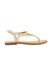 Sandalias planas nude con diseño de tira entre los dedos, que presentan tachuelas metálicas en las correas. La suela es de color marrón claro con una textura suave. Correa ajustable con hebilla.