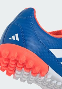 Blue synthetic athletic shoe with a textured upper, orange accents, and a distinctive outsole featuring conical studs for traction.