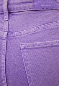 Fioletowe dżinsy z widocznym szwem, metka z napisem "Bershka" oraz detal z przednią kieszenią. Materiał ma teksturowane wykończenie.