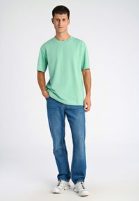 Camiseta de algodón verde menta con cuello redondo, combinada con unos clásicos pantalones de mezclilla azules y zapatillas blancas, con un diseño sencillo y un ajuste relajado.