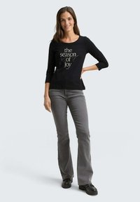 Black 3/4 sleeve T-shirt with "the season of joy" text in white, paired with gray flared jeans and black platform shoes. Simple, casual design.