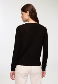 Czarny dzianinowy sweter z okrągłym dekoltem, prążkowanymi mankietami i dołem. Tekstura jest miękka, z lekko luźnym krojem z tyłu.