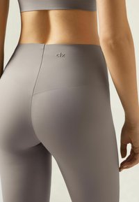 Legginsy z wysokim stanem w jasnoszarym kolorze, wykonane z elastycznego materiału. Charakteryzują się bezszwowym wzornictwem oraz wytłoczonym logo z tyłu.