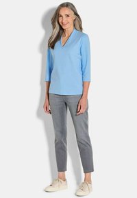 Lichtblauw V-hals top met driekwartmouwen, gecombineerd met grijze slim-fit broek en crèmekleurige sneakers. Glad textuur en eenvoudig ontwerp.