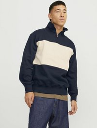 Sudadera de forro polar con parte superior en azul marino, medio en crema y parte inferior en azul marino. Cuenta con cuello con cremallera, puños acanalados y texto "ORIGINALS" grabado.