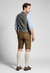 Gilet grigio, camicia a quadri blu, pantaloni corti in pelle marrone, calze crema fino al ginocchio e scarpe marroni. Presenta una cerniera laterale e cuciture decorative.