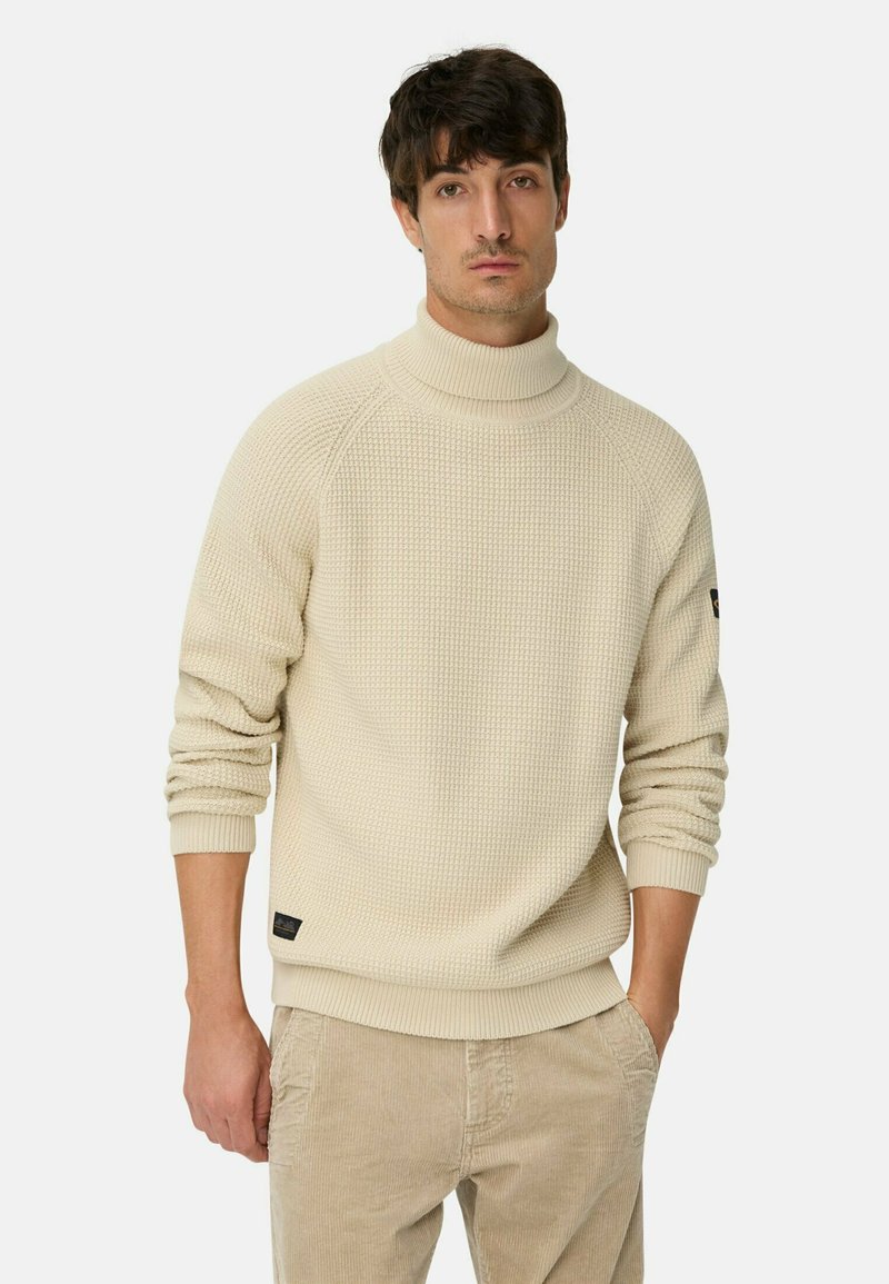 Cremfarbener Rollkragenpullover mit einem strukturierten Strickmuster, mit Rippbündchen und Saum, getragen über beigen Cordhosen.