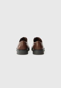 Zapatos de cuero marrón con una superficie suave, punta redonda y suela de goma negra. Diseñados con costuras mínimas y un tacón bajo.