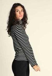 Maglione a collo alto a righe bianche e nere con maniche lunghe; design aderente e tessuto morbido, abbinato a pantaloni neri.