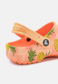 Oranžové dřeváky s třpytivým páskem, zdobené motivy ananasu a listů. Vyrobené z lehkého materiálu s texturovanou podrážkou a detailem ve tvaru kruhového loga.