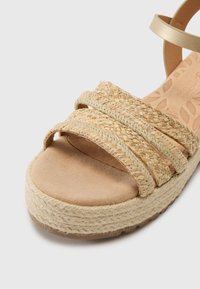 Beige platform sandal featuring braided natural fiber straps and a soft suede footbed. Accented with a textured midsole and rubber outsole.