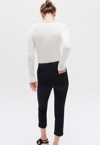 Vit ribbad tröja med långa ärmar, i kombination med svarta byxor av ankle-length med sidslitsar. Svarta skor fullföljer outfiten.