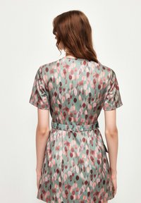Robe à manches courtes en tissu vert présentant un motif floral en rose, rouge et violet, avec une taille ajustée et une jupe évasée.