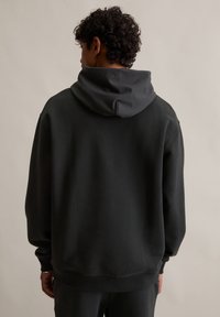 Ciemnoszary pulower z kapturem o miękkiej fakturze, z dużym kapturem, obniżonymi ramionami oraz ribbami przy mankietach i dolnym wykończeniu.