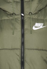 Chaqueta acolchada de color verde oliva con cremallera negra, capucha ajustable y logotipo de Nike en blanco en el lado izquierdo. Tejido texturizado e insulated.