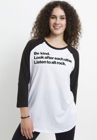 Biała i czarna koszulka z długimi rękawami w stylu raglanowym, z dużym czarnym napisem: "Bądź miły. Troszcz się o siebie nawzajem. Słuchaj alt rocka."
