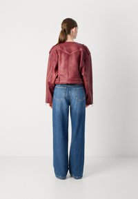 Burgundi odinė striukė su petnešomis ir sutrumpintu dizainu, derinama su šviesiai mėlynomis plačiomis kelnėmis ir lygiu paviršiumi.