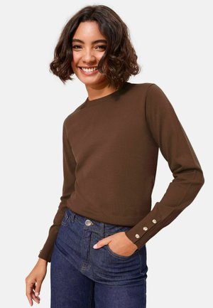 Pruun kootud kampsun pikkade varrukatega, soonikkoes äärega ja kolme dekoratiivse nupuga kummalgi mansetil. Ühildatud siniste kõrge vöökohaga teksadega.