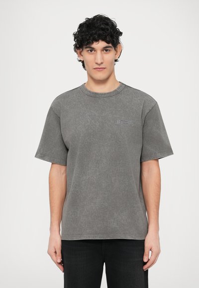 Graues übergroßes T-Shirt aus Baumwollmischung mit Rundhalsausschnitt, kurzen Ärmeln und einem dezenten Logo auf der linken Brustseite. Glatte Textur.