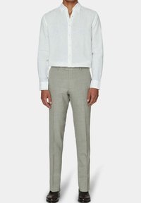 Weißes Leinenhemd mit Button-Down-Kragen, kombiniert mit hellgrauen maßgeschneiderten Hosen mit dezentem Karomuster und schmaler Passform.