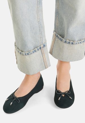 Čierne semišové baletky majú zaoblenú špičku, malú mašľu s kovovými akcentmi a sú skombinované s roztrhnutými svetlomodrými džínsami.
