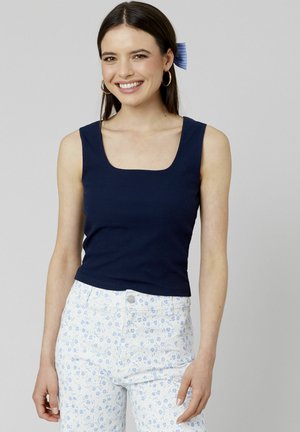 Débardeur côtelé marine avec un décolleté carré. Associé à un pantalon à imprimé floral clair. Design simple, coupe ajustée, matériau en coton.