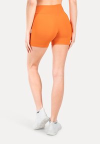Pantalones cortos deportivos de color naranja con una cintura alta, textura suave y ajuste ceñido, combinados con zapatillas blancas con acentos negros.