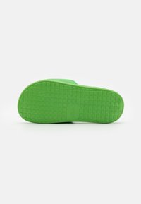 Semelle de chaussure en caoutchouc vert avec surface texturée présentant un motif en grille et un petit logo en relief dans la zone du cou-de-pied.