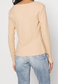 Beige långärmad topp med vid halsringning och slät textur, matchad med ljusblå denimjeans med bakfickor och en blekt design.