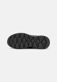 Semelle de chaussure en caoutchouc noir avec un motif texturé comprenant des formes ovales et circulaires pour une meilleure adhérence. Le design inclut des accents de marque subtils.