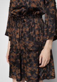 Robe avec motif camouflage abstrait noir et marron, avec une taille élastique et des manches amples et fluides.