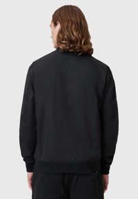 Schwarze Bomberjacke mit glatter Textur, elastischen Bündchen und tailliertem Bund. Sie zeichnet sich durch ein einfaches Design ohne sichtbare Logos oder Muster aus.