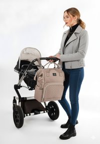 Passeggino grigio chiaro con seduta nera, borsa per pannolini trapuntata beige, e stivali neri indossati da una persona in giacca grigia aderente e top scuro.