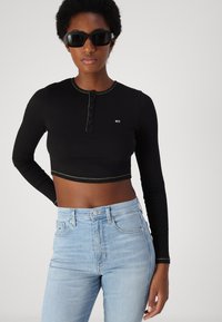 Sort ribbet crop top med lange ærmer, knaplukning og kontrasterende syninger, parret med lyseblå højtaljede jeans.
