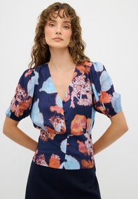 Blumenbluse in Marineblau mit lebhaften orange, pink und aqua Mustern. Verfügt über einen tiefen V-Ausschnitt, Puffärmel und Knopfdetail an der Vorderseite.