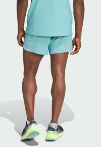 Turkosa träningsshorts med lös passform, parat med flerfärgade löparskor med lätt sula och strukturerad mönster.