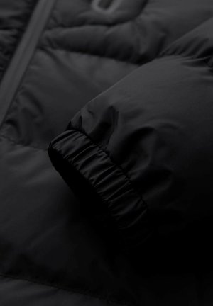 Detalje af sort dunjakke med en struktureret, quiltet overflade og en elastisk, rynket ærmekant. Glat, nylonlignende stof.