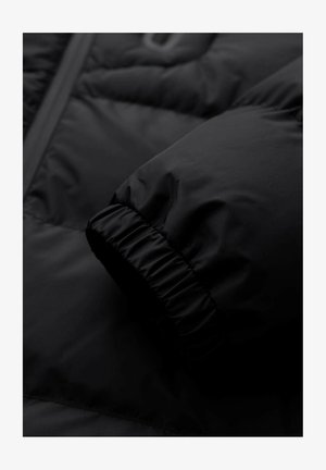 Detalje af sort dunjakke med en struktureret, quiltet overflade og en elastisk, rynket ærmekant. Glat, nylonlignende stof.