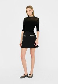 Schwarzes, geripptes Oberteil mit kurzen Ärmeln, kombiniert mit einem schwarzen A-Linien-Rock mit dekorativen Nähten an den Taschen. Getragen mit flachen Schuhen.