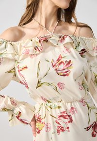 Robe à imprimé floral à épaules dénudées en tissu léger. Dotée d'un col à volants, d'une taille élastique et de manches amples avec des poignets évasés.